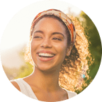 Profile photo of a woman smiling. She is wearing a headband and white tank top.